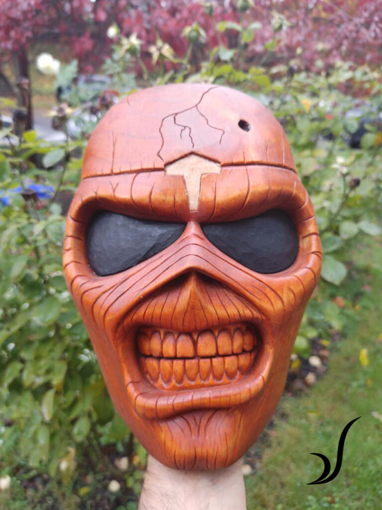 Hand carved by a Tlingit artist, an Alder mask depicting Eddie the mascot for band Iron Maiden with logo embedded from Bifrost Blacksmithing